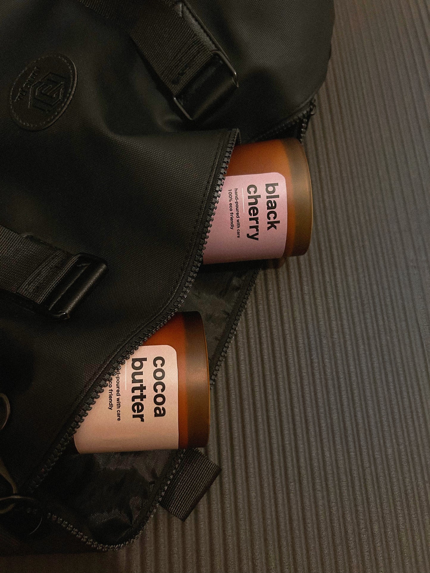 Two brown containers labeled 'cocoa butter' and 'black cherry' peeking out from a black bag on a textured surface.