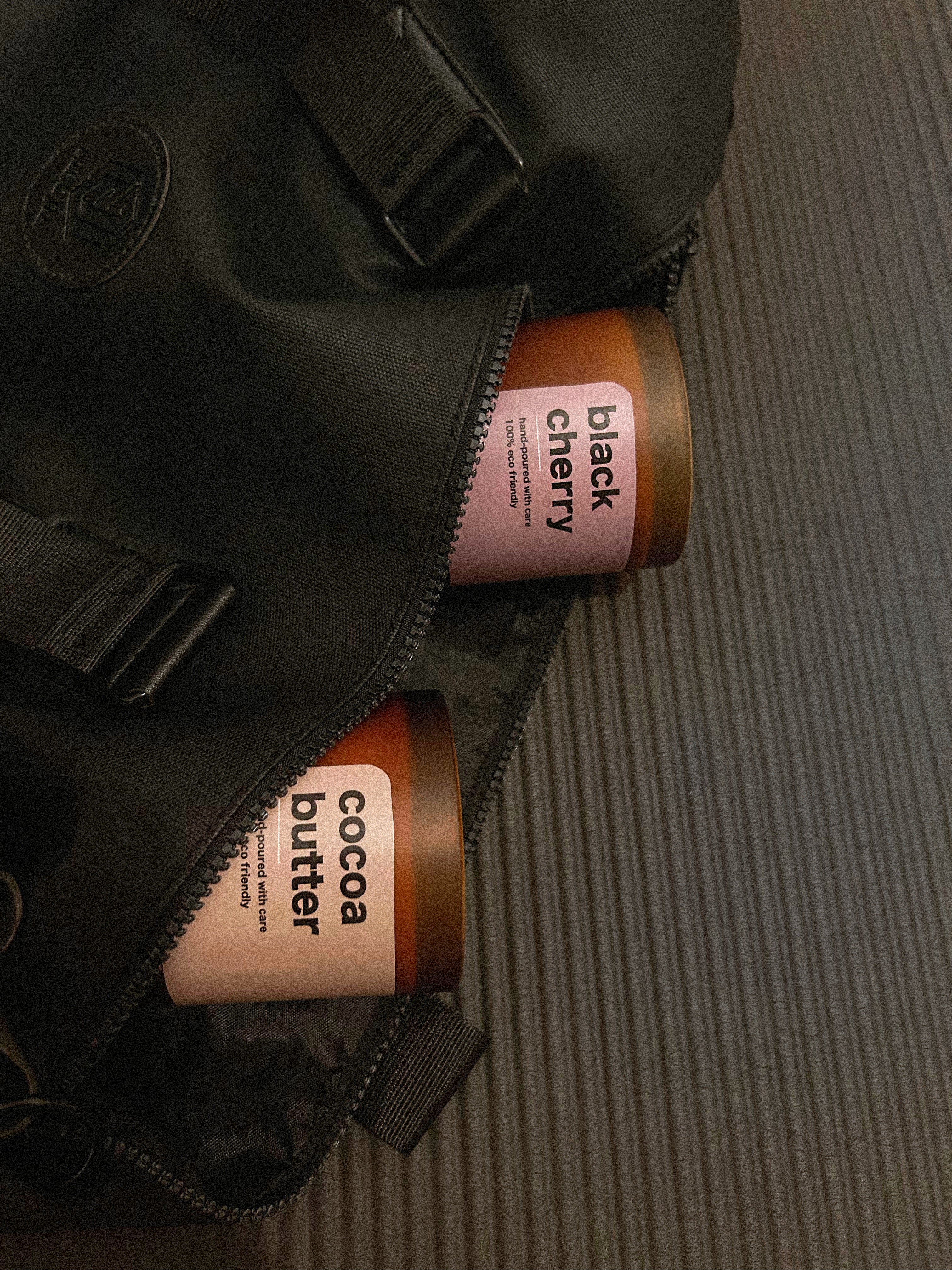 Two brown containers labeled 'cocoa butter' and 'black cherry' peeking out from a black bag on a textured surface.